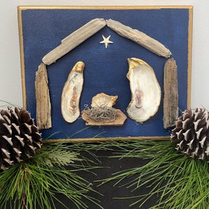 May include: A blue canvas painting depicting a nativity scene with a gold star above the manger. The manger is made of driftwood and oyster shells. The painting is framed in gold.