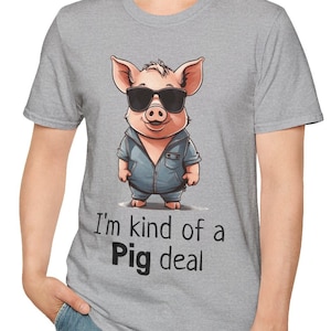 Puede incluir: Una camiseta gris con un cerdo de dibujos animados que lleva gafas de sol y una chaqueta vaquera azul. El texto "I'm kind of a Pig deal" está impreso en la camiseta.