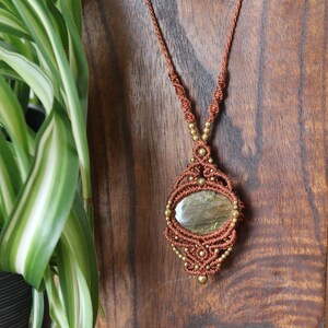 May include: A brown macrame necklace with a gold-toned metal bead accent and a green gemstone pendant.