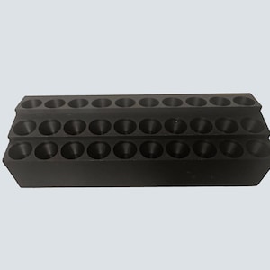 May include: A black, tiered organizer with three rows of circular holes. The organizer is made of a solid, dark material and is designed to hold small items. The holes are evenly spaced and appear to be of uniform size.