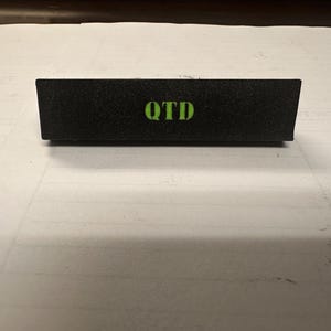 May include: A black rectangular sign with the word "OTD" printed in green letters.