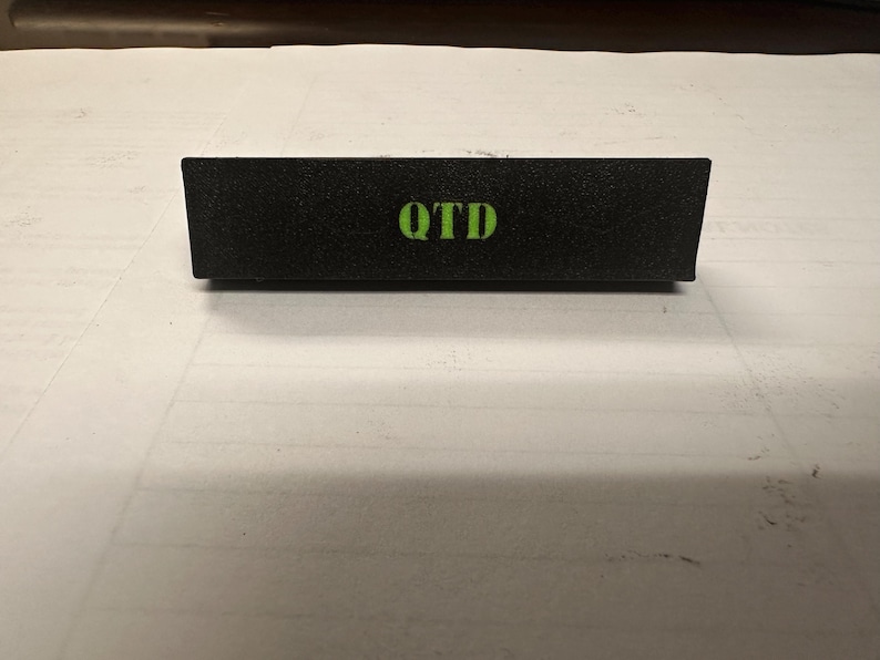 May include: A black rectangular sign with the word "OTD" printed in green letters.