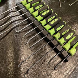 May include: A black tool holder with 10 green and black handled tools. The tools have a metal hook on one end and a flat edge on the other end.