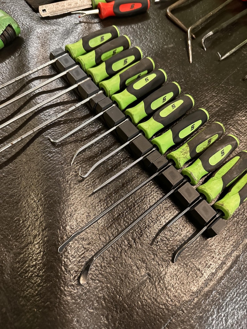 May include: A black tool holder with 10 green and black handled tools. The tools have a metal hook on one end and a flat edge on the other end.
