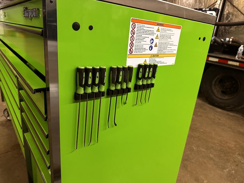 May include: A bright green metal toolbox with multiple drawers. The toolbox has a magnetic strip on the side with a variety of tools, including screwdrivers and pry bars. The toolbox has a warning label with safety instructions.