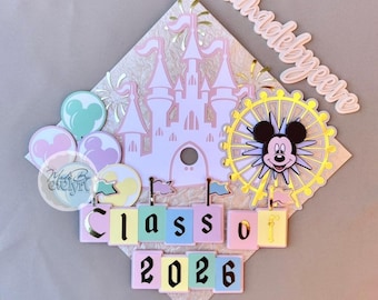 May include: A diamond-shaped graduation cap topper featuring a light pink castle, a yellow Ferris wheel with a mouse character face, pastel balloons, and layered blocks spelling out Class of 2026. The text Madebyevelyn appears in script.