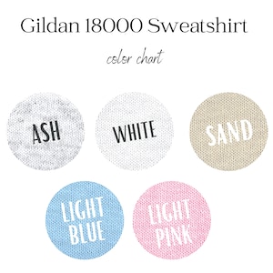 May include: A color chart for a Gildan 18000 Sweatshirt. The chart displays five color options: Ash, White, Sand, Light Blue, and Light Pink. Each color is presented in a circular swatch with the color name printed in a contrasting color.