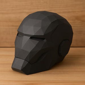 Op de afbeelding: Een zwarte, geometrische Iron Man-helm, met een polygonale vormgeving. De helm is matzwart en staat op een houten oppervlak. Het ontwerp is hoekig en gedetailleerd, met gedefinieerde vlakken en randen, wat het een moderne, artistieke uitstraling geeft.