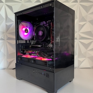 May include: A black desktop computer tower with a transparent glass side panel, featuring an internal cooling fan with pink and purple LED lighting, a black CPU cooler, and a graphics card labeled GeForce GTX with MSI branding visible inside.