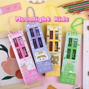 May include: Four colourful pencil sets with cartoon characters and the text "Moonlight Kids". Each set contains pencils, an eraser, and a sharpener. The sets are in pink, purple, yellow, and green, with matching handles.
