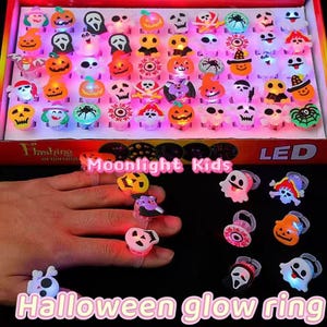 May include: A box filled with Halloween-themed LED light-up rings. The rings feature various designs, including pumpkins, ghosts, spiders, and skulls. The rings are in a variety of colors and are designed for children. The text "Halloween glow ring" is visible.