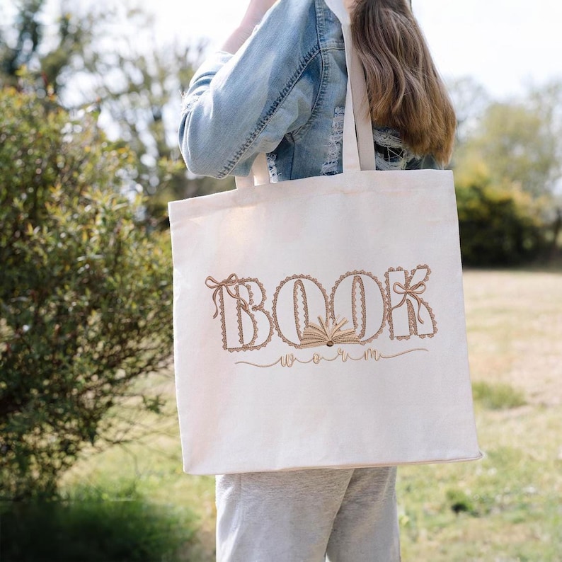 Pu&ograve; includere: Borsa tote color crema con la scritta "BOOK" e "worm" in marrone. Le lettere sono decorate con pizzo e fiocchi, con un libro aperto al centro. La borsa &egrave; portata da una persona.
