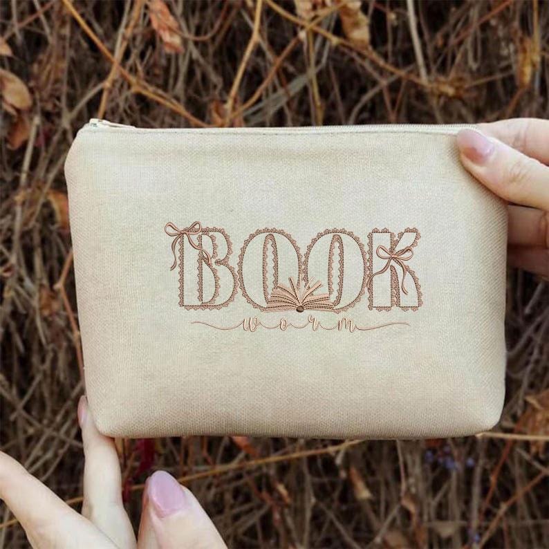 Pu&ograve; includere: Un astuccio in tela beige con chiusura a cerniera. L'astuccio presenta le parole ricamate "BOOK worm" in un carattere decorativo. Il design include un'illustrazione di libro aperto.