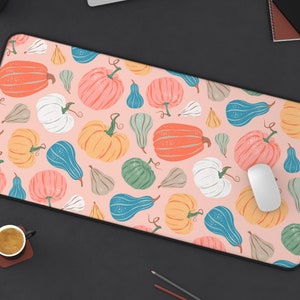 May include: A pink and white mouse pad with a pattern of orange, yellow, and green pumpkins. The mouse pad is on a black surface with a laptop, a notebook, and a potted plant.