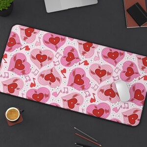 May include: A pink desk mat featuring a repeating pattern of red and pink heart-shaped vinyl records, white flowers, and musical notes. The mat has a black border and is designed for use with a computer mouse.