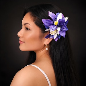 May include: A hair accessory featuring a large, multi-layered flower in shades of deep purple, white, and yellow. The petals have a textured, realistic appearance with a central yellow stamen and a smaller white orchid-like bloom tucked underneath.