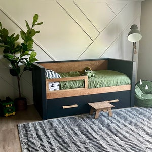 May include: A black and wood daybed with a green mattress and a black and white patterned rug. The daybed has a storage drawer and a small wooden stool.