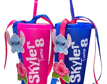 May include: Two glittery plastic tumblers with lids and straws, one hot pink and one royal blue. Each features a cartoon character decal, a pink hibiscus flower, and white text reading Skyler Turns 8, accented with tied blue and pink ribbons.