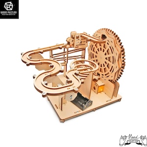 May include: Wooden marble run toy with a large gear wheel and multiple tracks. The toy is made of natural wood and has a battery compartment on the bottom.