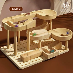 Pode incluir: Brinquedo de pista de mármore de madeira com vários níveis e pistas. O brinquedo apresenta um acabamento em madeira clara, com bolinhas coloridas rolando pelas pistas. A base é uma placa de madeira perfurada. O texto "Style 2" é visível.