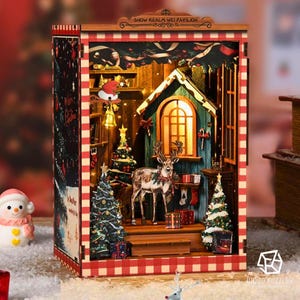Puede incluir: Diorama de madera con temática navideña que representa una cabaña con un ciervo, árboles de Navidad y regalos. El diorama tiene un borde a cuadros rojos y blancos y el texto "SNOW REALM WEI PAVILION".