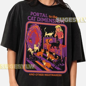 May include: Black t-shirt featuring a colorful graphic with the text "PORTAL to the CAT DIMENSION" and "AND OTHER NIIGITMARESS!". The graphic depicts a portal with cats and a girl.