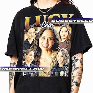 May include: Black t-shirt with a vintage-style graphic of Lucy Chen from the TV show "The Rookie". The graphic features multiple images of Lucy Chen in different poses, with the text "Lucy Chen" in a gold font.
