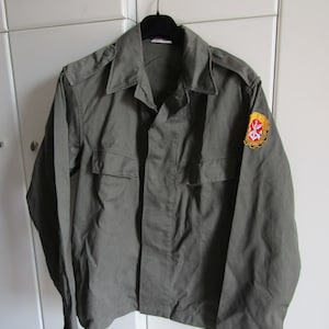 Może przedstawiać: Zielona kurtka wojskowa z naszywką na prawym rękawie. Naszywka jest żółta z czerwonym kotwicą i innymi szczegółami.