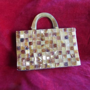 Può includere: Una piccola borsa rettangolare realizzata con un mosaico di pezzi di conchiglia marroni e dorati. La borsa ha un manico in legno.