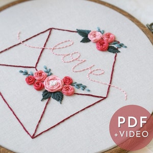 Puede incluir: Arte de bordado en aro con un diseño de sobre rojo que presenta la palabra "love" en escritura cursiva. El sobre está decorado con flores rosas y rojas y hojas verdes. El aro está hecho de madera y tiene un acabado marrón. El texto "PDF + VIDEO" es visible en la esquina inferior derecha.