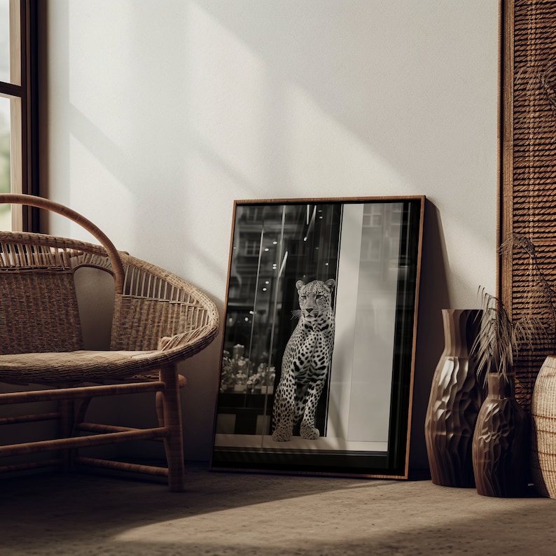 May include: A black and white photograph of a leopard in a window. The leopard is looking directly at the camera. The photograph is framed in a dark wood frame and is hanging on a white wall.