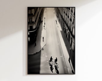 Op de afbeelding: Zwart-witfoto van een Parijse straatbeeld. Twee mensen fietsen over straat, met gebouwen aan beide kanten.