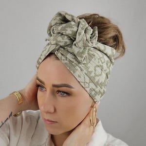 Könnte beinhalten: Ein grünes und weiß gemustertes Turban-Haarband mit einem Knoten oben. Das Haarband ist aus einem weichen, dehnbaren Stoff.