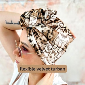 Könnte beinhalten: Ein brauner und weißer gemusterter Samt-Turban mit einem Knoten oben. Der Text "flexible velvet turban" befindet sich unten im Bild.