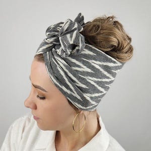 Könnte beinhalten: Ein graues und weiß gemustertes Stirnband, das oben auf dem Kopf zu einem Knoten gebunden ist. Das Stirnband ist aus einem weichen, dehnbaren Stoff.