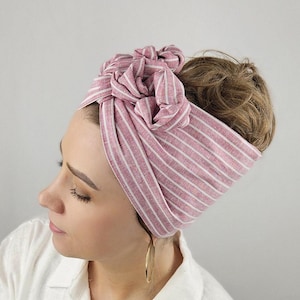 Könnte beinhalten: Ein rosa-weiß gestreiftes Stirnband, das oben auf dem Kopf zu einem Knoten gebunden ist. Das Stirnband ist aus einem weichen, gewebten Stoff.