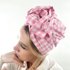 Könnte beinhalten: Ein rosa-weiß kariertes Kopftuch. Der Stoff ist auf dem Kopf gewickelt und gebunden, wodurch ein stilvoller und strukturierter Look entsteht. Das Kopftuch ist aus weichem Stoff.