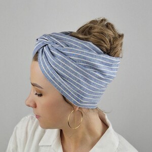 Könnte beinhalten: Ein blaues und weiß gestreiftes Turban-Haarband aus Leinen. Das Haarband ist oben auf dem Kopf zu einem Knoten gebunden.