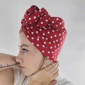 Könnte beinhalten: Ein roter Turban mit weißen Punkten. Der Turban ist gewickelt und oben auf dem Kopf verknotet. Die Person trägt goldene Creolen.