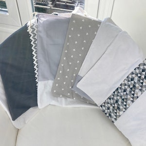 May include: Five gray and white fabric drawstring bags with different patterns. The bags are made of a soft, cotton fabric and have a drawstring closure. The patterns include a chevron pattern, a heart pattern, a geometric pattern, and a solid gray pattern.