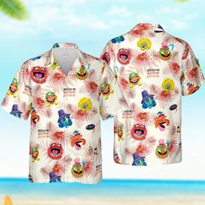 Puede incluir: Una camisa blanca de botones con estampado tropical que presenta varios personajes de los Muppets, incluidos Animal, Cookie Monster y Elmo. La camisa tiene un fondo blanco con flores rosas y hojas verdes. El texto "MAYHEM! MAYHEM! MAYHEM!" se repite en todo el estampado.