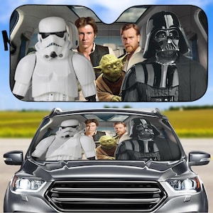 May include: A car sunshade featuring characters from Star Wars. The sunshade is black with a white border and shows Darth Vader, Yoda, Luke Skywalker, Han Solo, and a Stormtrooper.