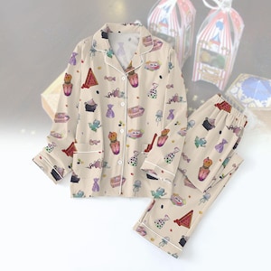 May include: A beige pajama set with a long-sleeved top and pants. The fabric features a whimsical print of potion bottles, candy, and other magical items.