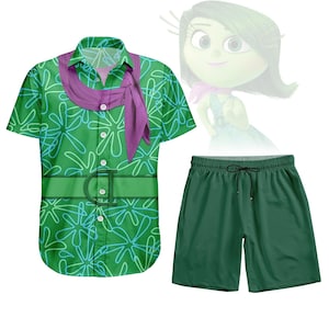 Puede incluir: Conjunto de camisa y pantalón corto verdes. La camisa presenta un estampado floral con detalles azules y una bufanda morada. El pantalón corto es verde liso. Un personaje de dibujos animados está en el fondo.