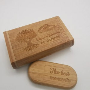 Puede incluir: Una caja rectangular de bambú y una memoria USB ovalada de bambú a juego. La caja presenta un árbol grabado, dos anillos entrelazados y el texto "Dario e Eleonora 05/08/2022". La memoria USB tiene grabado el texto "The best moments".