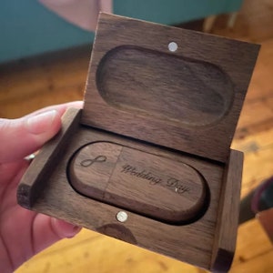 May include: A dark brown wooden rectangular box with a hinged lid containing a matching wooden USB flash drive. The flash drive is engraved with an infinity symbol and the text Wedding Day in a cursive script. The box features a magnetic closure.
