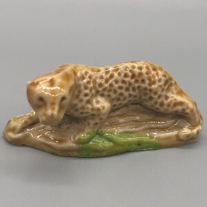 May include: A small ceramic figurine of a brown and white leopard crouching on a green base.