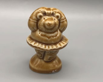 May include: A brown ceramic figurine of a bear wearing a tutu and holding its arms up above its head.