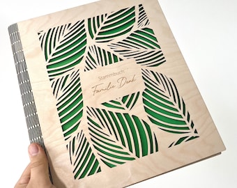 May include: A wooden scrapbook with a green leaf design and the text "Stammbuch Familie Denk" on the front.