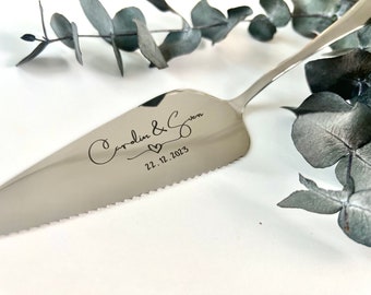 May include: Silver cake server with a serrated edge. The server is engraved with the text "Carolyn & Gwen" and the date "22.12.2023".